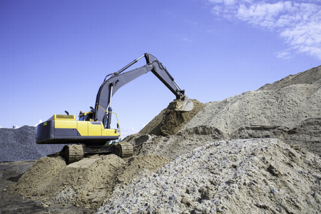 A large yellow excavator on the road construction site picks up and pours sand rubble stones in a quarry construction machinery excavator digsの写真素材