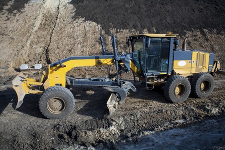The construction machine Motor Grader level the ground with the construction of a new asphalt road a large powerful construction equipment with a shovel for laying roads and leveling the groundの写真素材