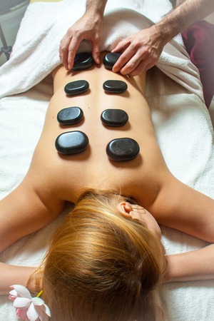Beauty treatments, a woman relaxing at a health spa while having a hot stone treatment and massage...
