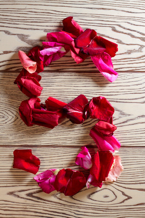 Alphabet of rose petals - S letter laid out from the petals of red roses and pink flowers on a wooden light backgroundの写真素材