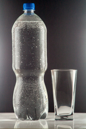 Pure mineral water pouring from a bottle into a glass. bottle of clear drinking cold mineral water with gas in isolation on the background next to a glass transparent glassの写真素材