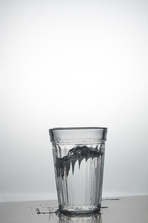 Transparent glass cup with a pouring bubbling cold fresh water with bubbles and dropsの写真素材
