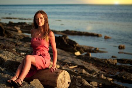 Olginka, RUSSIA - August 11 ,2017: A romantic girl in a green dress is sitting on the rocks near the sea shore at sunset in the resort town of Olginka on the Black Sea coastのeditorial素材