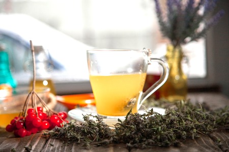 Herbal tea from the viburnum decoction of red sea buckthorn berries and thyme in a transparent glass mug in the village on a wooden tableの写真素材