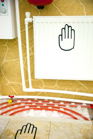 Heating in a home. A radiator with thermal head and water tap of a warm floor under a laminate of a parquet and a tile Floor heating pipe. Installation of engineering systems in a building.の写真素材