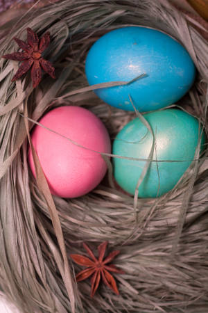 Colorful easter eggs in basket in the hay of the green grass straw bundle dietary delicious gift on wooden table. Top view with copy spaceの写真素材
