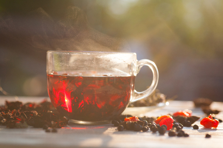 Fresh red chrysanthemum tea with rose petals of hibiscus in a transparent glass mug on a white wooden table with red berries and thymeの写真素材