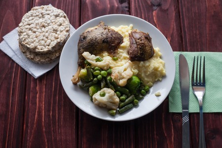 Fried chicken with potatoes and vegetables cauliflower and beans on a plate standing on a wooden tableの写真素材