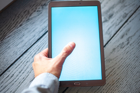 A modern digital tablet with a bright with a white screen lying on an old vintage wooden desk with penの写真素材