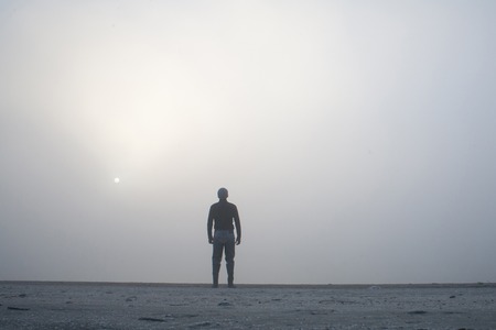 Beautiful freedom moment and peaceful atmosphere - Man standing alone on edge of footbridge and staring at lake. Mist over water. Foggy air early chilly morning in autumn.の写真素材