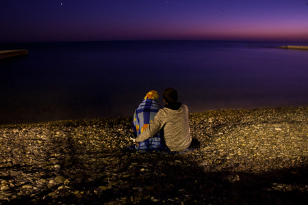 couple of lovers sitting on the seashore at night under the light of the moon and stars in a romantic settingの写真素材
