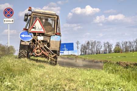 Tractor with a mechanical mower mowing grass on the side of the asphalt road. Road services are engaged in landscaping around roads.の写真素材