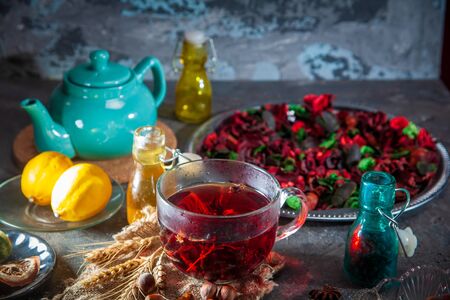 Red Hot Hibiscus tea in a glass mug on a wooden table among rose petals and dry tea custard with metallic heartの写真素材