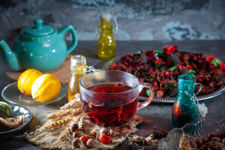Red Hot Hibiscus tea in a glass mug on a wooden table among rose petals and dry tea custard with metallic heartの写真素材