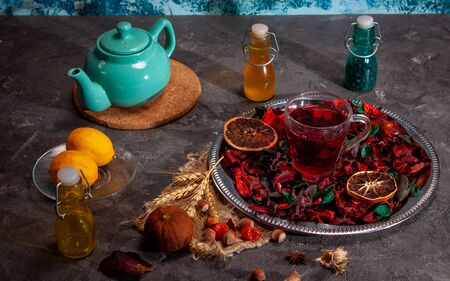 Red Hot Hibiscus tea in a glass mug on a wooden table among rose petals and dry tea custard with carcadeの写真素材