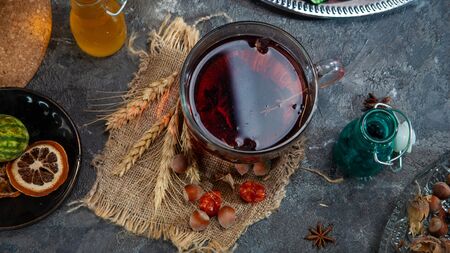 Red Hot Hibiscus tea in a glass mug on a wooden table among rose petals and dry tea custard with...