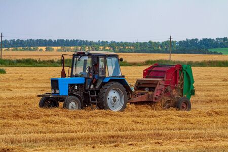 A tractor with a trailed bale making machine collects straw rolls in the field and makes round large balesの写真素材
