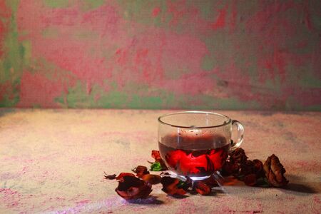 Red Hot Hibiscus tea in a glass mug on a wooden table among rose petals and dry tea custard with carcadeの写真素材