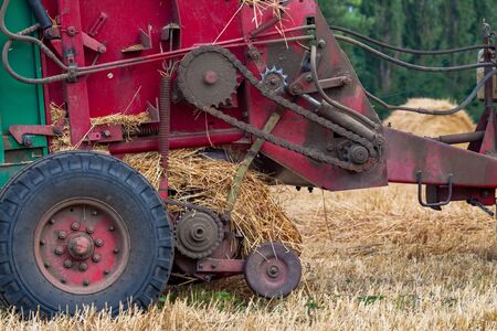 A tractor with a trailed bale making machine collects straw rolls in the field and makes round large balesの写真素材