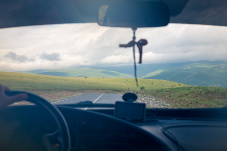 driver behind the wheel of a car in the mountains, perspective view. Driver with hands on the steering wheel. Traveling by car along a mountain road.の写真素材