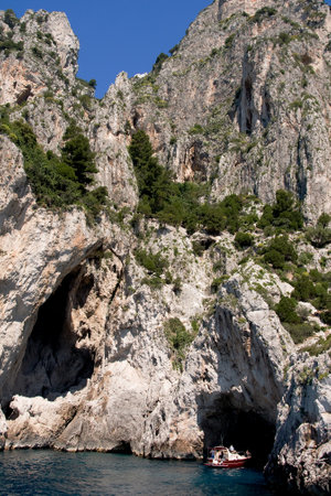 CAPRI, ITALY, MAY 11, 2012: Small motorboat with tourists goes near coastal rocks near the small cave of Capri islandのeditorial素材