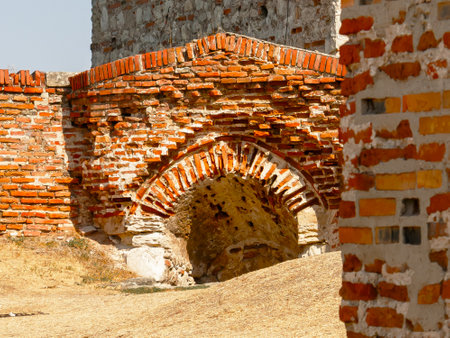 An intricately designed brick archway stands within the remnants of ancient ruins, illuminated by...