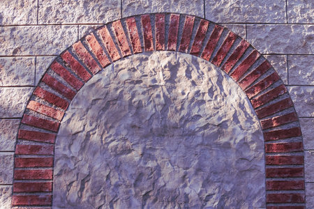 Close-up of a textured stone wall with a half-arch brick design, showing detailed craftsmanship and interplay of light and shadow that highlights the warm tones and geometric structure.の写真素材