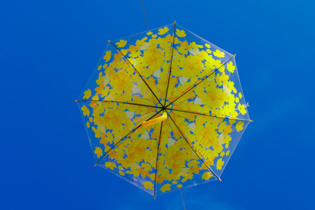 Bottom view of a transparent umbrella adorned with vivid yellow maple leaves suspended against a deep blue sky, creating a cheerful and artistic outdoor autumn atmosphere.の写真素材