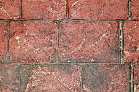 Close-up of an aged red brick pavement showing detailed texture, cracks, and weathering, forming a rustic surface pattern ideal for backgrounds, architecture, or construction design concepts.の写真素材