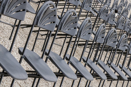 Perspective view of multiple rows of identical black chairs lined up on a textured stone surface. The composition emphasizes rhythm, geometry, and organization, capturing a calm pre-event atmosphere in daylight.の写真素材