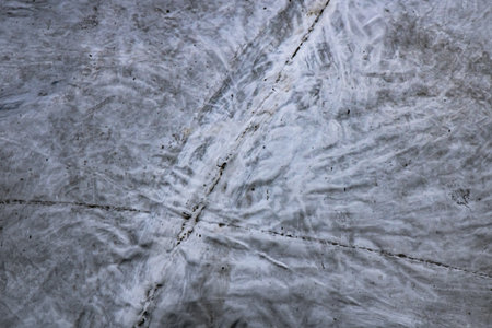 Detailed close-up of a gray concrete surface showing intersecting cracks, subtle patterns, and surface wear under daylight â capturing the raw urban texture of pavement and construction material.の写真素材