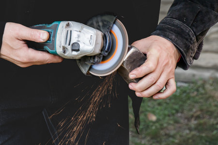 Close-up of a craftsman working with an angle grinder, producing bright sparks as he shapes a piece of metal. The image captures precision, skill, and manual craftsmanship in action.の写真素材
