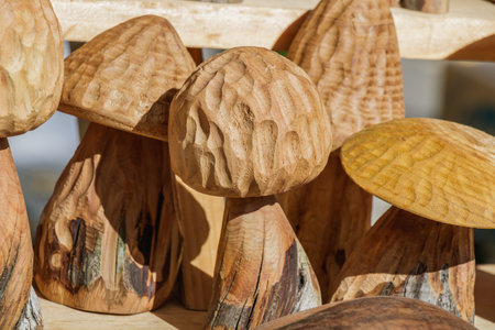 Carved wooden mushrooms with organic shapes and detailed textures displayed at a local artisan fair. The sunlight accentuates the craftsmanship, highlighting the warm tones and wood grain patterns.の写真素材