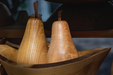 Two handcrafted wooden pears with smooth texture and visible wood grain displayed in a rustic bowl at an artisan market. The soft lighting enhances the natural tones and craftsmanship.の写真素材