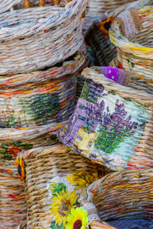 Decorative woven baskets featuring sunflower and lavender patterns are stacked at a local market. The natural textures and vivid colors highlight creativity, craftsmanship, and rustic artistry.の写真素材