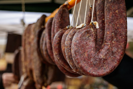 Rows of traditional cured sausages hanging from strings at a local outdoor market. The image highlights the artisanal preparation and authentic food craftsmanship typical of handmade regional products.の写真素材