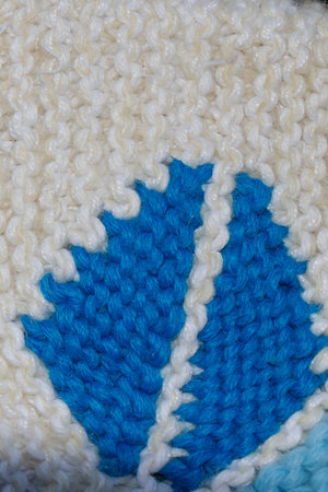 Macro view of a blue leaf motif knitted into white wool fabric, highlighting detailed yarn texture,...