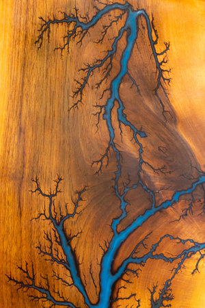 Close-up of polished wood featuring branching blue resin inlays that resemble lightning or tree roots, highlighting organic patterns and handcrafted artistic woodworking.の写真素材