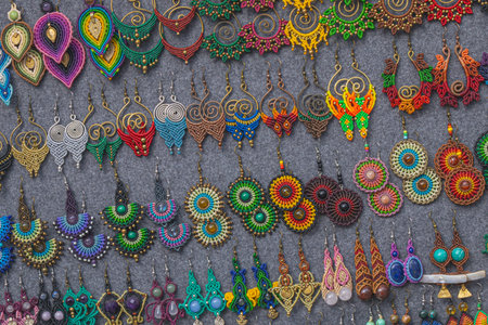 Wide view of colorful handmade earrings arranged on fabric display at a craft market, showing...