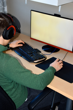 Gamer or streamer in earphones with microphone sits at home in dark room and plays with friends on networksの写真素材