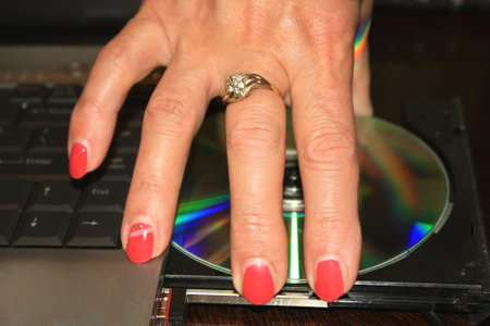 woman's hand with red nails taking DVD disc from PC.の写真素材