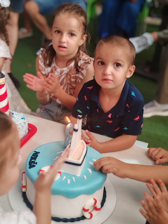 Group of children at birthday party blowing out candles on cake in kindergartenの写真素材