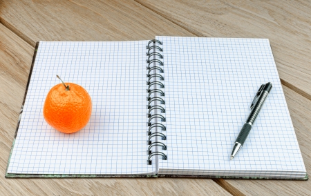 Notebook with a pencil and an orange on a wooden tableの写真素材