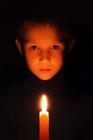boy with burning wax candles in their hands in the darkの写真素材
