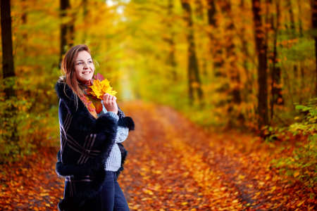 Girl with leaves in her hands in the autumn forest posing for the camera.