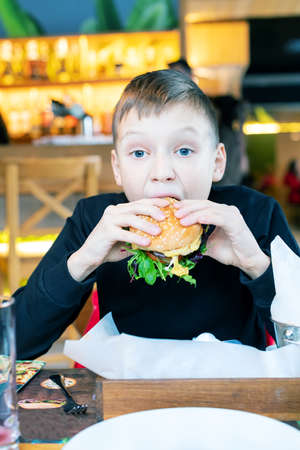 cute boy refilling a hamburger in a restaurant trying to eat itの写真素材
