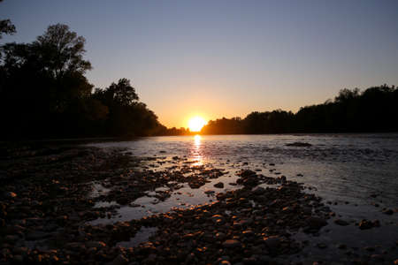 Beautiful, golden sunset on the stone, Sava river shore in the peaceful, forest environment around the riverbank while the sun is reflecting in water surfaceの写真素材