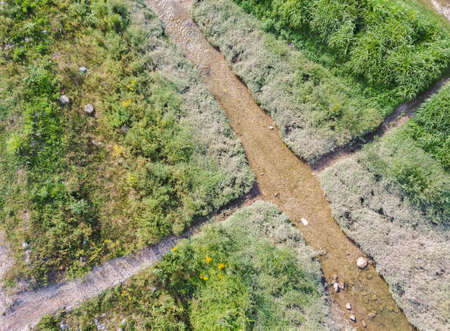 Drone aerial view of small field dirt pathway crossing the shallow stream that flows to the Sava river  nearby on the outskirts of Zagreb city, Croatiaの写真素材