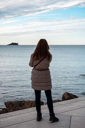 Rovinj, Croatia-January 6th, 2022: Woman standing on the shore of Mulini beach at the town of...