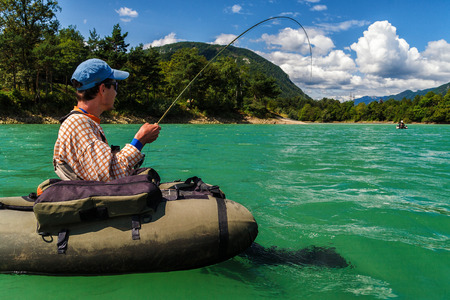 Fisherman sitting in bellyboat and fighting with big trout on lake in Jesenice, Slovenia. Still...